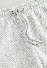 Lichtgrijze shorts met een geometrisch patroon, voorzien van een elastische tailleband, zilverkleurige hardware en een trekkoord voor aanpassing.