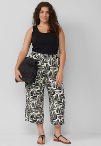 Zwarte tanktop gecombineerd met crèmekleurige en zwarte gebloemde cropped broek. Houdt een gestructureerde zwarte tas vast, draagt platte sandalen met een subtiele accent.