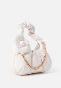 Sac à main blanc froncé avec un détail de fleur rembourrée sur la poignée et une courte bandoulière chaîne dorée sur fond uni.