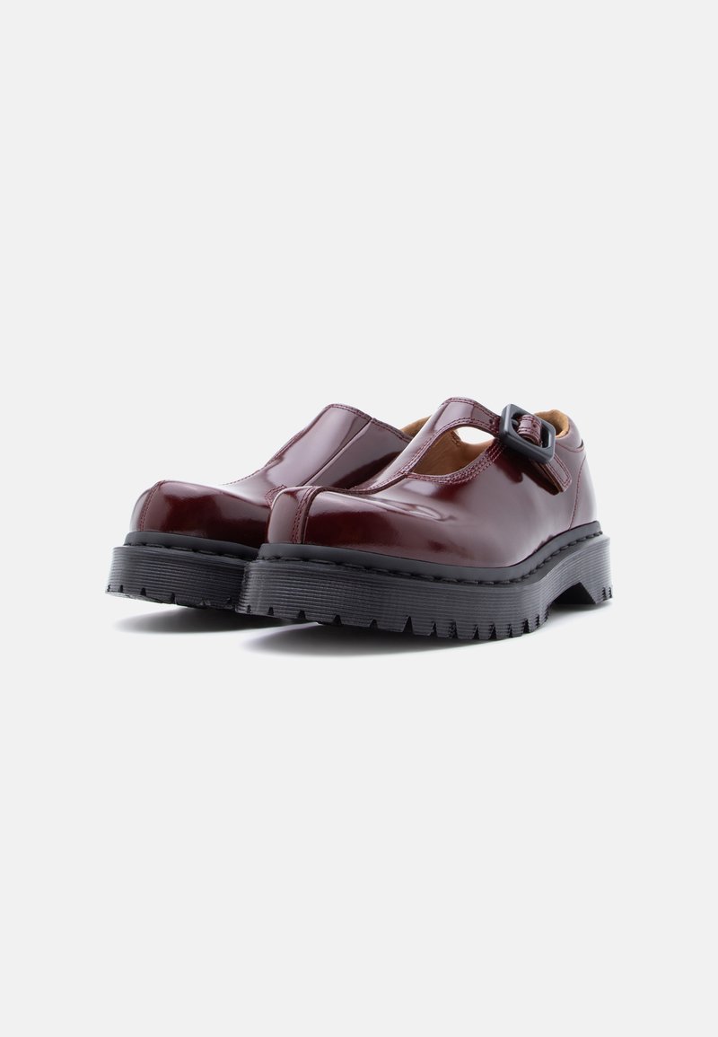 Chaussures à brides en T en cuir verni bordeaux avec une semelle noire épaisse, ornées d'une boucle et d'un design ajouré. Texture lisse, forme arrondie des orteils.