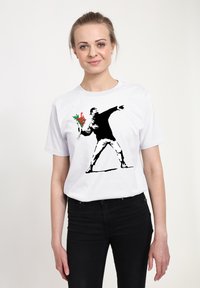 Bílé tričko s černobílým šablonovým motivem postavy házející kytici červených a zelených květin.