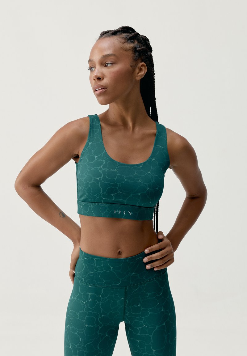 Teal urheiluliivi, jossa on teksturoitu kuvio, leveät olkaimet ja sopiva muotoilu. Yhdistetty vastaaviin teksturoituihin leggareihin.