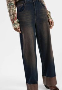 Jeans in denim a gamba larga di colore blu scuro con una texture sbiadita. Presentano dettagli in marrone sui orli e un classico design a cinque tasche.