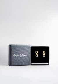 Guldtonet uendelighedsbånd øreringe præsenteret i en sort fløjlsklædt smykkeboks med en struktureret sort yderside. "Sofia Milani Jewels" logo.