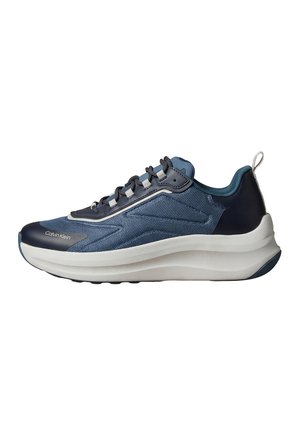 Blaue und marineblaue Sneaker mit niedrigem Schaft, weißer dicker Sohle, Schnürverschluss und Calvin Klein-Logo nahe der Spitze auf weißem Hintergrund.
