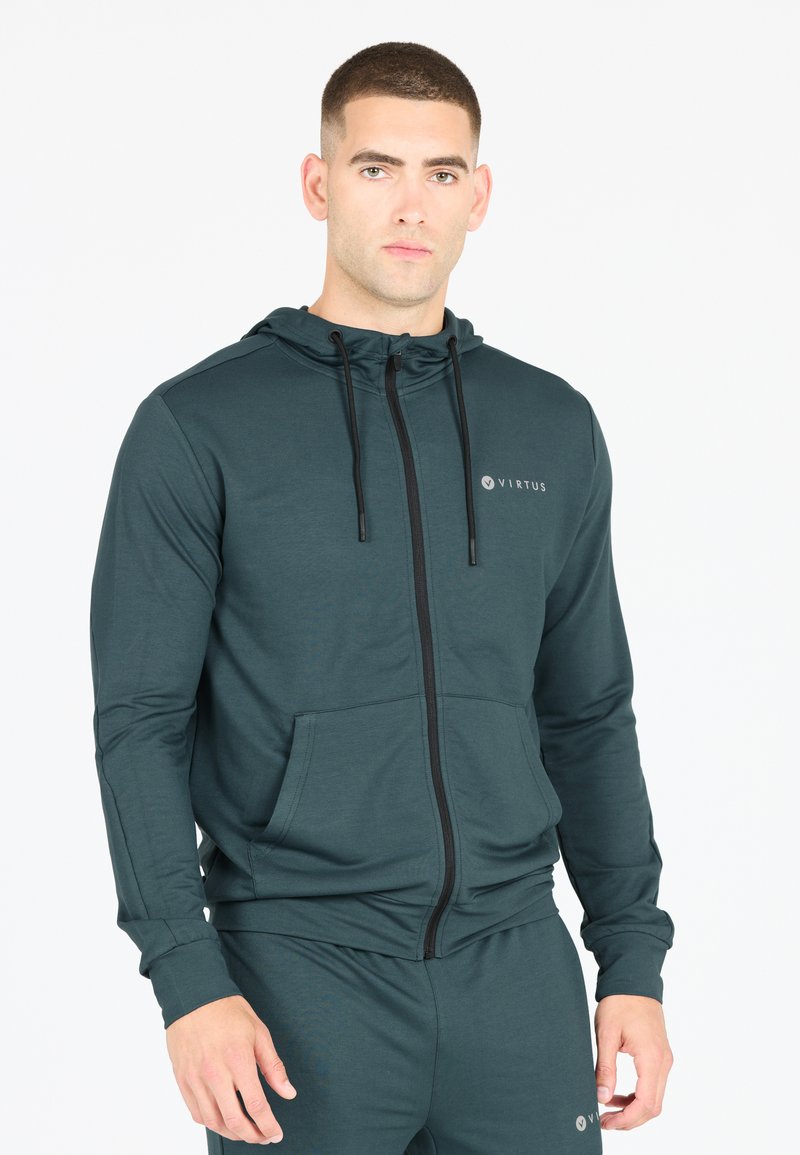 Mörkgrön zip-up hoodie i mjukt tyg, utrustad med en huva, justerbara snörr, framfickor och en subtil logotyp på bröstet.