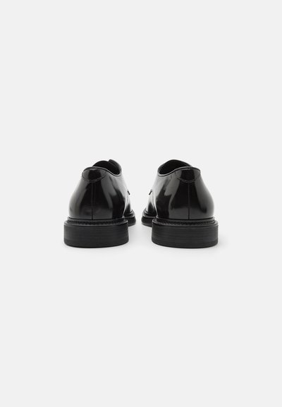 Scarpe in vernice nera con una finitura liscia, punta tonda e un tacco in gomma nera basso. Cuciture semplici e senza dettagli hardware visibili.