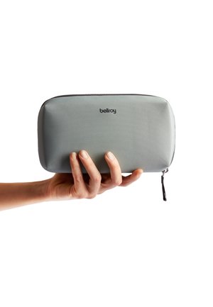 Gray textured zippered pouch held by a hand. Features a smooth surface, rounded edges, and a small zipper pull tab. Logo printed on the front.