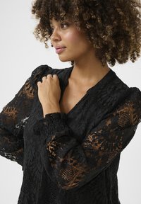 Black lace blouse featuring intricate floral patterns, puffy sleeves, and a V-neckline; sheer and textured fabric adds depth.