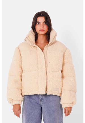 Beige cropped Pufferjacke aus flauschigem Sherpa-Material, mit einem einfarbigen tanfarbenen oberen Teil, Reißverschluss und elastischen Ärmelbündchen.