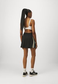 Černá sportovní sukně s bílými vertikálními pruhy, doplněná bílým sportovním podprsenkami. Modelka má na sobě černé tenisky a bílé ponožky. Dlouhé vlasy má stažené do culíku.