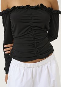 Top negru, cu umeri descoperiți, cu guler volanat, design cu corp plisat, textură netedă, asortat cu pantaloni scurți albi, elastici, cu talie înaltă.