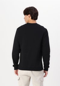 Zwarte sweatshirt met ronde hals, lange mouwen en geribbelde manchetten, gemaakt van zachte stof, gedragen over lichtbeige broek.