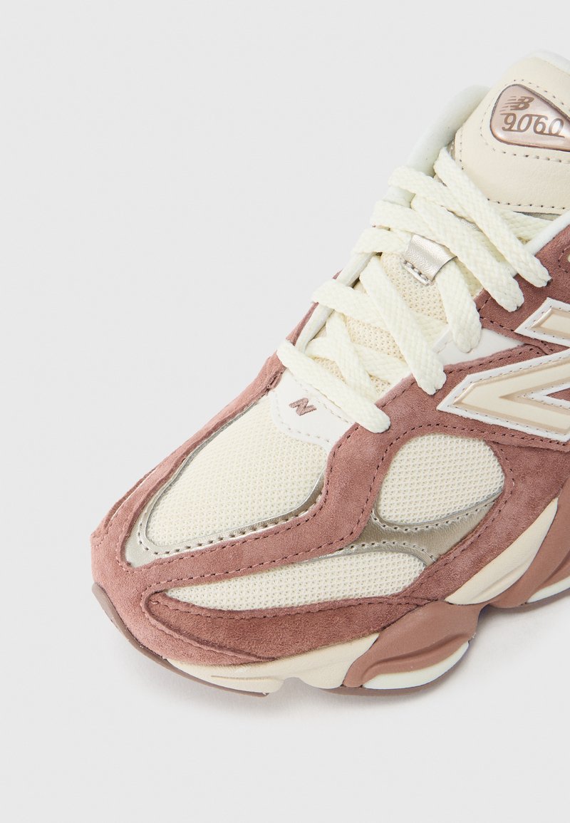 Hellrosa und cremefarbener Sneaker mit einem Mesh-Obermaterial, Wildleder-Overlays und strukturierten Akzenten. Auffälliges New Balance-Logo an der Seite.