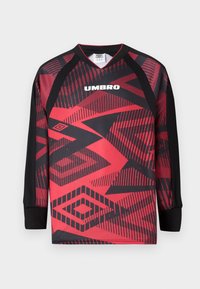 Hosszú ujjú Umbro sportmez piros és fekete geometrikus mintákkal, fekete mandzsettákkal, fehér alapon.
