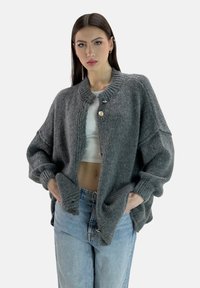Cardigan grigio lavorato a maglia con scollatura rotonda, maniche oversize e chiusura frontale con bottoni. Morbido al tatto, con polsini e orlo a coste.