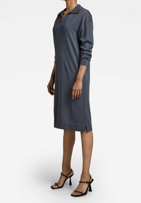 Grå stickad klänning med polo-krage, långa ärmar, sidofickor vid fållen och ribbade manschetter, i kombination med svarta remmar högklackade sandaler.