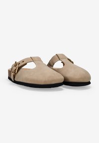 Zapatos slip-on de ante beige con punta redondeada, lado cortado y detalle de hebilla ajustable. Tacón parecido a corcho con suela de goma negra.