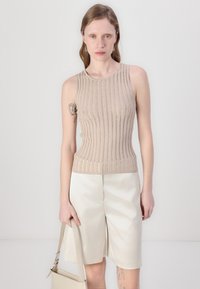 Bež ribaga kootud tank top, mis on kombineeritud kreemivärvi lühikeste pükstega, omades kitsast lõiget ja ümmargust kaelust. Käes on väike käekott.