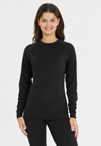 Sort langærmet top lavet af glat stof, med en rund hals og raglanærmer, parret med matchende sorte leggings.