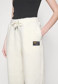 Fleece-Sweatpants in Off-White mit einem Zugbandbund, Seitentaschen und einem schwarzen Etikett mit orangefarbenem und weißem Text. Strukturiert Oberfläche.