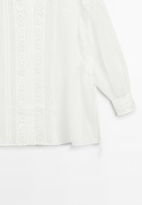 Witte lange mouwen blouse met bloemenkant-detail aan de voorkant, knoopsluiting en manchetten met bijpassende kanten afwerking.