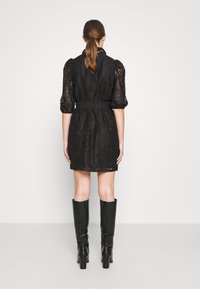 Vestito di pizzo nero con maniche a sbuffo, vita aderente e gonna svasata. Presenta un colletto alto ed è abbinato a stivali neri fino al ginocchio.