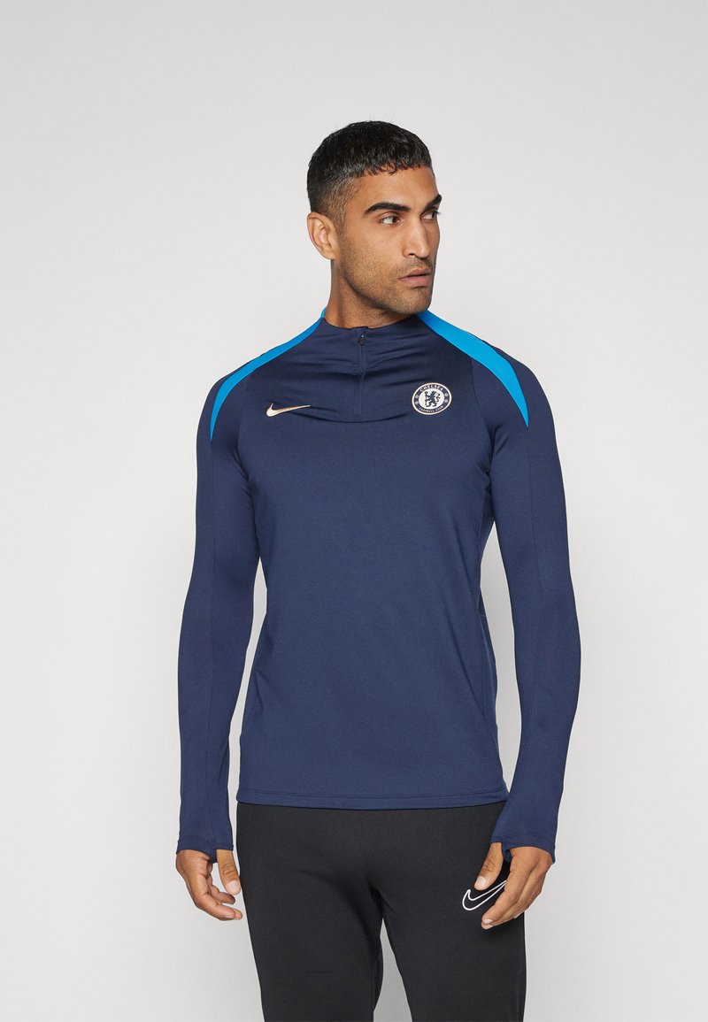 Top atletico a maniche lunghe navy con mezza zip, accenti azzurri brillanti sulle spalle e logo del Chelsea FC. Realizzato in un tessuto liscio e elastico.