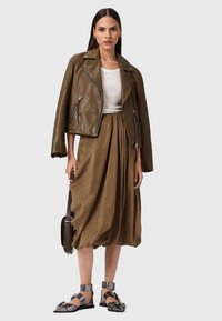 Giacca da moto in pelle oliva, camicia fitted bianca, gonna fluida oliva e sandali grigi con fibbie. Semplice borsa a tracolla nera.