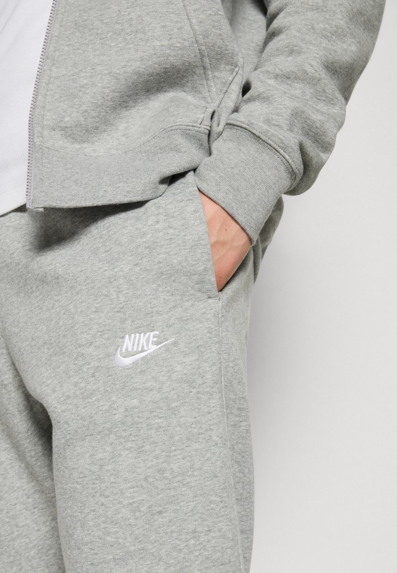 Sweatshirt et pantalon de survêtement Nike gris, fabriqués en tissu doux. Présente un logo Nike brodé blanc sur le pantalon et des poignets côtelés.