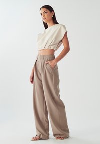 Top corto beige con orlo elastico, abbinato a pantaloni larghi marrone chiaro con tasche e una texture liscia.
