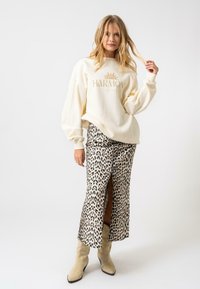 Sweatshirt crème avec le texte "HARMONY" et un graphique de soleil, associé à une jupe en imprimé léopard avec une fente sur le côté. Des bottines beiges à la cheville complètent le look.
