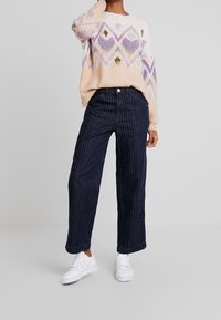 Light pink sweater with diamond pattern in purple and metallic accents, paired with navy blue pinstriped wide-leg pants and white sneakers.