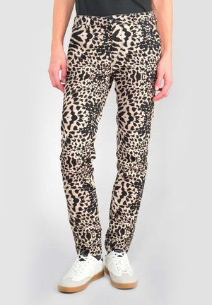 Pantalons imprimés léopard en beige et noir, avec une coupe slim, fermeture à bouton et poches avant. Portés avec des baskets blanches.