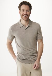 Grå kortärmad polo med krage, två knappar och en subtil textur. Bärs tillsammans med ljusa shorts, modellen ler självsäkert.