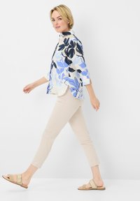 Lichte blouse met bloemenpatroon in blauw en zwart, met 3/4 mouwen, gecombineerd met beige slim-fit broek en platte sandalen.