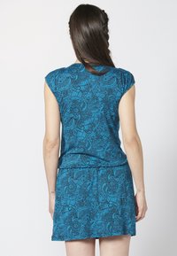 Lyhythihainen sininen mekko, jossa on kukka- ja abstrakteja kuvioita. Pehmeää kangasta, rento istuvuus, kapea vyötärö ja levenevä hame. Takakatsaus esitetty.