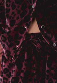 Burgundi sametist lounge-komplekt mustade leopardiplekkidega, millel on lahti istuv lõige, seotud talje ja metallist nööbid.