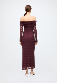 Off-shoulder burgundy lace dress with long, sheer sleeves; fitted silhouette; floral pattern; ankle-length with a scalloped hem. Silver heels.