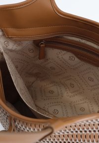Tan geweven handtas met een glad leren bovenkant en stoffen voering. Het interieur heeft een ritsvak en een herhaald logo-patroon op de voering.