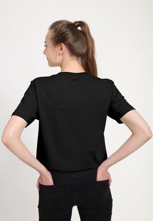 T-shirt en coton noir à manches courtes, avec un col rond et une coupe décontractée, vue de dos. Associé avec un pantalon noir.