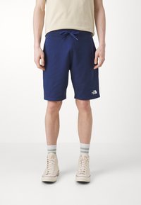Pantaloni corti blu navy realizzati in tessuto morbido, con una cintura elastica dotata di lacci e un piccolo logo bianco sul lato sinistro in basso.