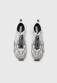 Des chaussures de sport blanches et grises avec une tige en mesh texturé, des lacets noirs, une semelle rembourrée et un logo distinctif sur la semelle intérieure.