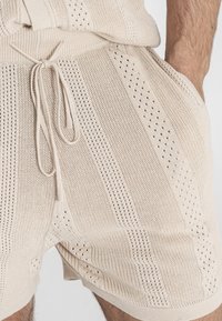 Gebreide shorts in lichtbeige garen, met verticale streepjespatronen en open mesh details. Voorzien van een verstelbare trekkoordtaille.