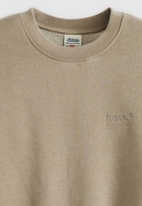 Beige crewneck sweatshirt gemaakt van zachte stof, met een geborduurd logo op de linkerborst en ribgebreide manchetten en halslijn.