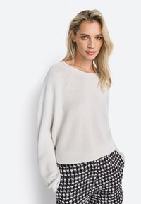 Jasnoszary, luźny sweter z szerokim dekoltem i miękką teksturą, zestawiony z spodniami w czarno-białą kratę houndstooth.