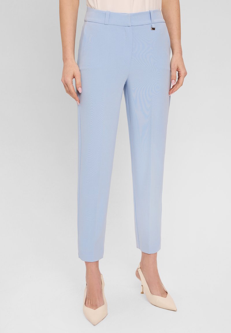 Błękitne, dopasowane spodnie o gładkiej fakturze, zwężających się nogawkach i subtelnym połysku. Posiadają pasek w talii z małym metalowym akcentem.