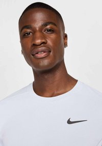 Balta Nike T-kreklu ar apaļu apkakli un īsām piedurknēm, ar melnu swoosh logotipu kreisajā krūšu daļā. Gluda auduma tekstūra.