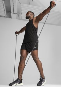 Top y shorts deportivos negros usados por una persona que utiliza bandas de resistencia. Incluye un diseño elegante y zapatillas deportivas negras con detalles en blanco.