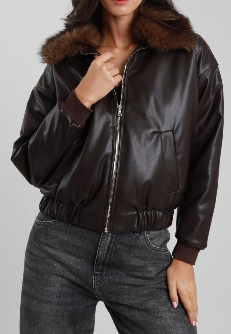 Giacca bomber in pelle marrone con colletto in pelliccia sintetica, chiusura con zip, polsini a coste e vita elastica. Presenta una tasca frontale.